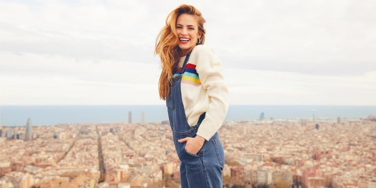 Red-head Woman wearing jean overalls with a beige sweater, outside