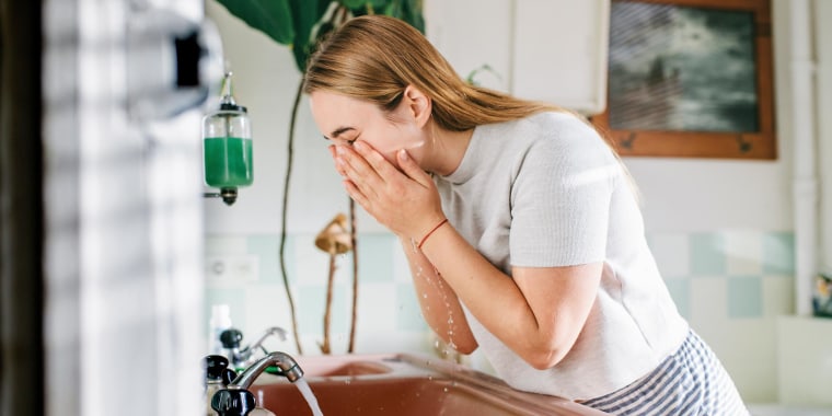 Woman washing her face, leaning over her sink, in the bathroom