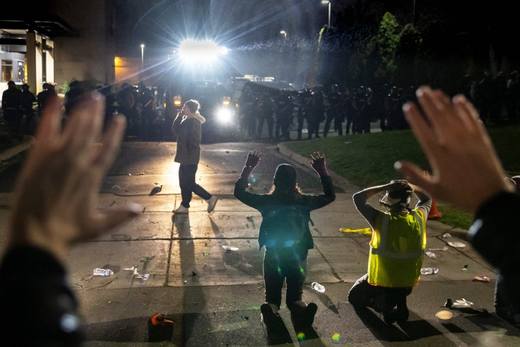 IMAGE: Protesters shout "Don't shoot" while kneeling and raising their arms in front of police officers at the Brooklyn Center Police Station 