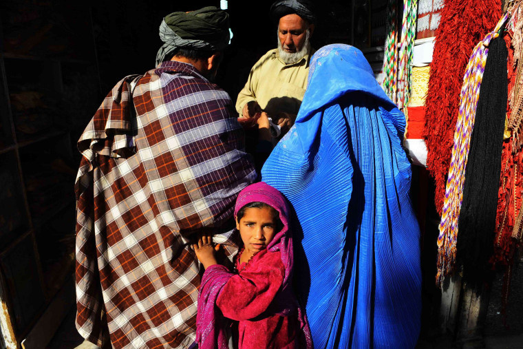 Image: An Afghan girl looks on as her parents shop in a market in Herat ahead of the Muslim feast of Eid al-Adha.