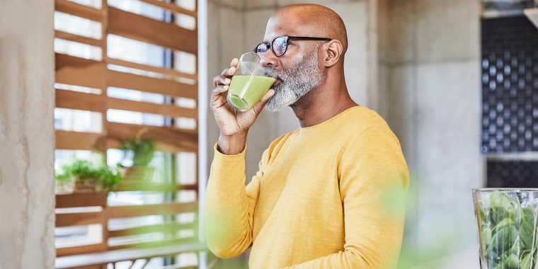 Man leaning on a counter drinking green juice