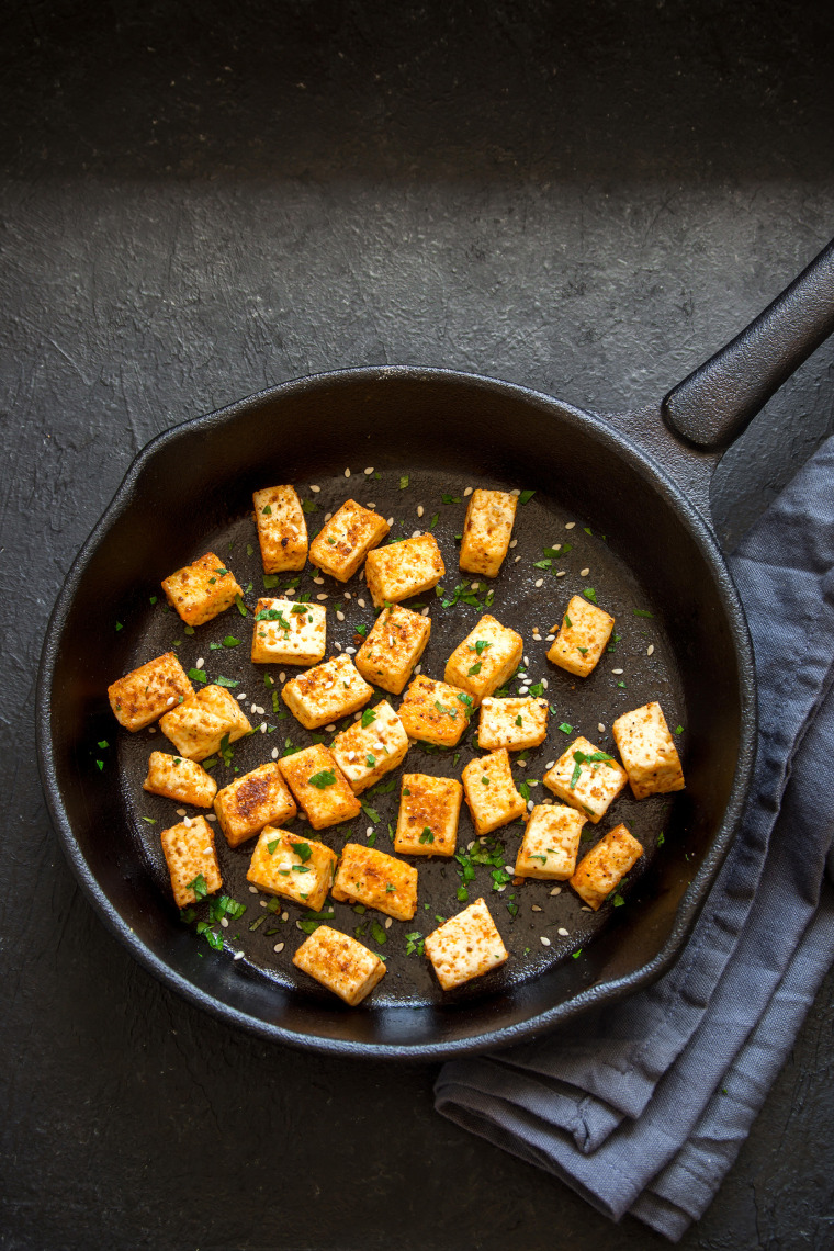 Fried tofu with sesame seeds and spices on cast iron pan, copy space. Healthy ingredient for cooking vegan vegetarian diet food. Roasted tofu over bla