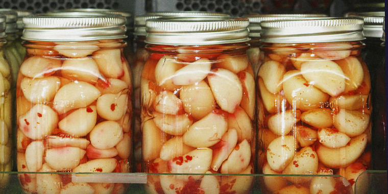 Homemade pickled garlic cloves preserved in mason jars with chopped chilli peppers - in a row