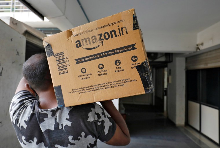 Image: An Amazon delivery worker carries a package to a customer at a residential apartment in Ahmedabad, India