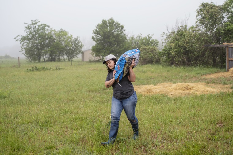 Carolina Mueller, 30, carries feed at Middle Ground Farm in Bastrop, Texas.