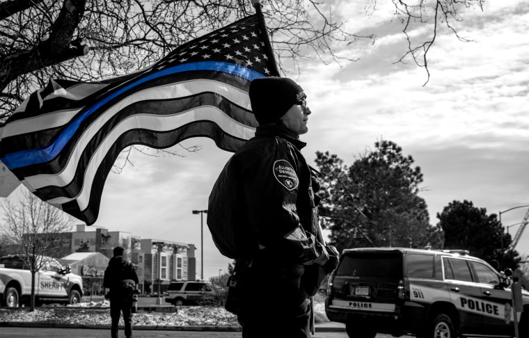 Image: A police officer with a Blue Lives Matter flag in a procession route during a memorial service.