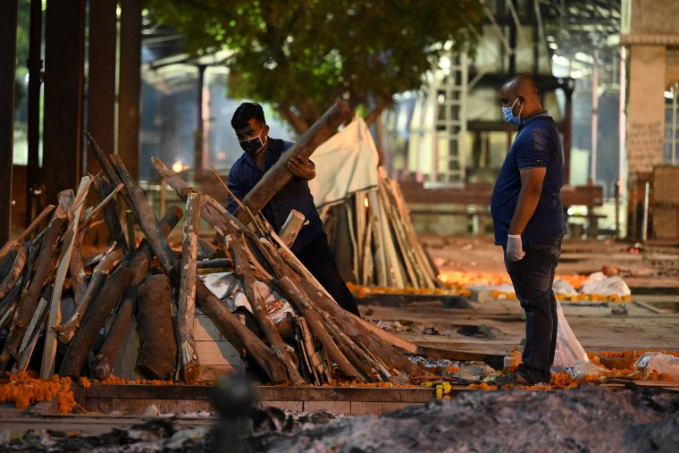 Image: A crematorium member of staff places fire wood on a pyre of a Covid-19 victim at Nigambodh Ghat Crematorium, on the banks of the Yamuna river in New Delhi