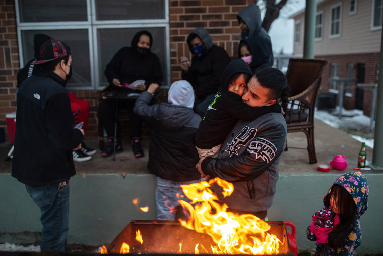 Image: Eric Traugott warms up his young son, Eric Traugott Jr., beside a fire, made from a discarded wooden armoire outside of their apartment in Austin, Texas, that remains without power on Feb. 17, 2021. (Tamir Kalifa/The New York Times)