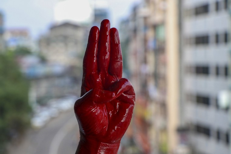 Image: An anti-coup protester shows the three fingered salute of resistance on his red painted hand in memory of protesters who lost their lives during previous demonstrations in Yangon, Myanmar