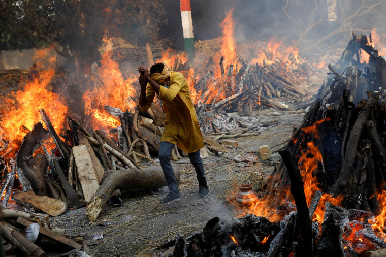 Image: A man runs past the burning funeral pyres of those who died from Covid-19 during a mass cremation in New Delhi