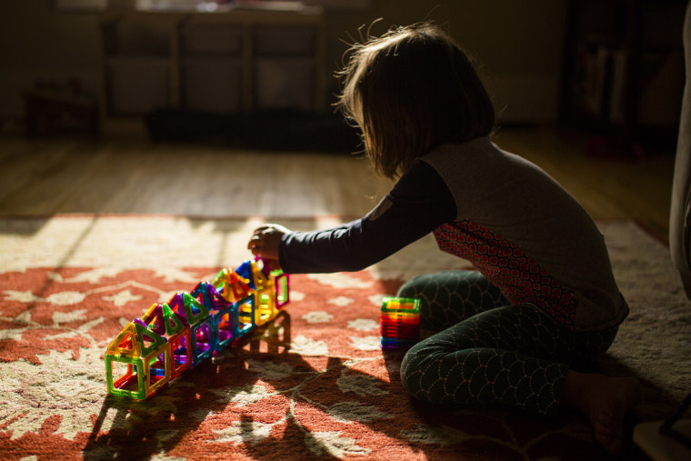 A child sits on the floor in golden morning light building with tiles