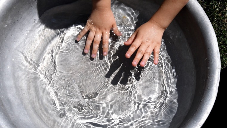 Kid clap and splash hands in clear water inside basin. Summer fun