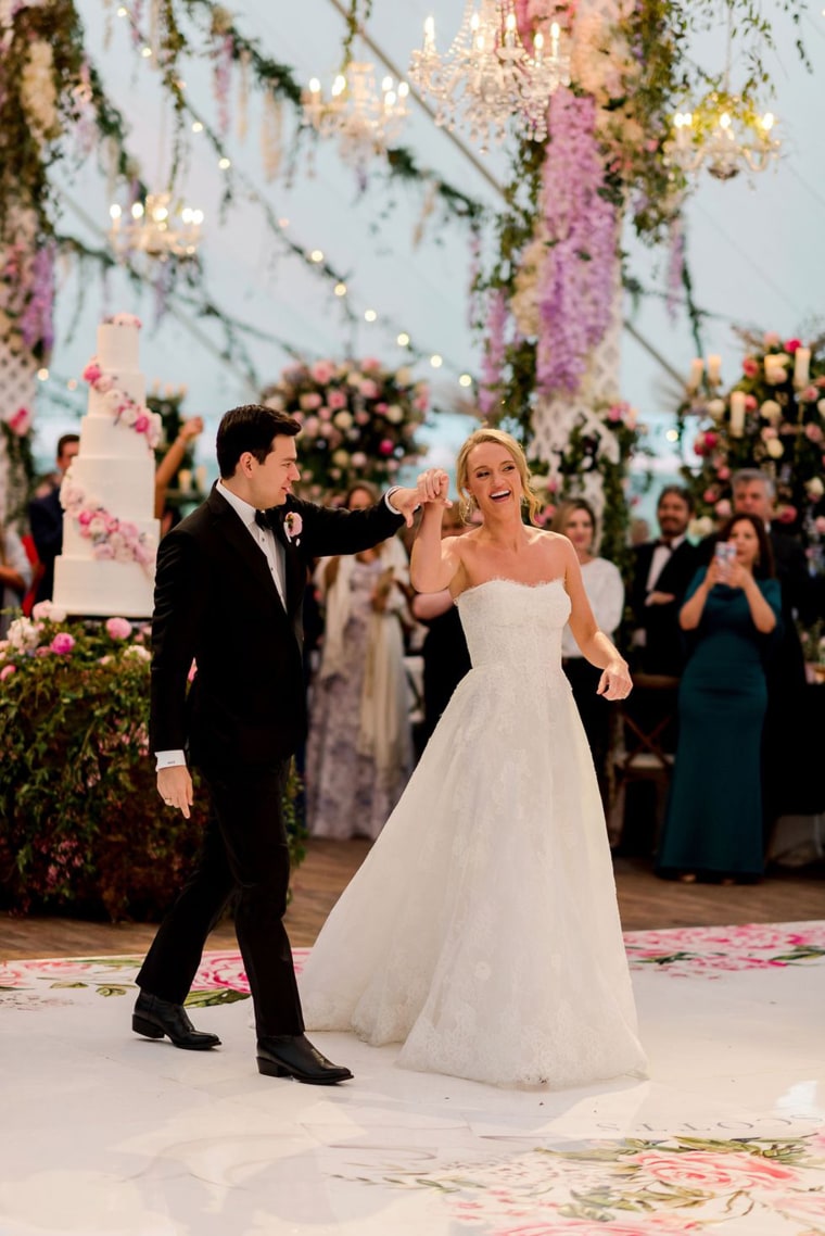 Alex Drummond in a white wedding gown dances with her new husband in a black suit on a dance floor under hanging purple flowers