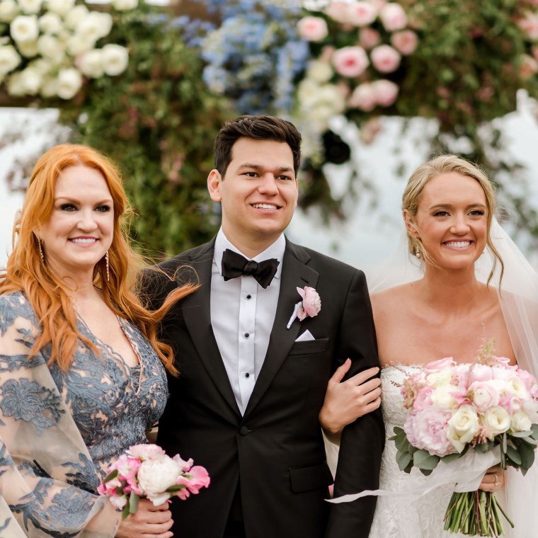 A mother with bright orange hair stands proudly next to a smiling bride and groom