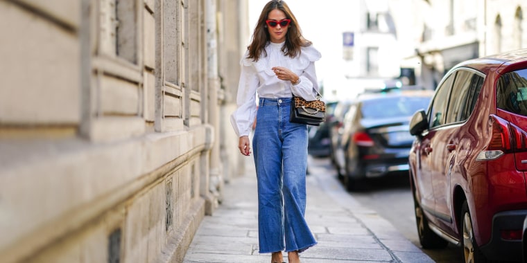 Woman walking down the street wearing flare jeans and a white shirt