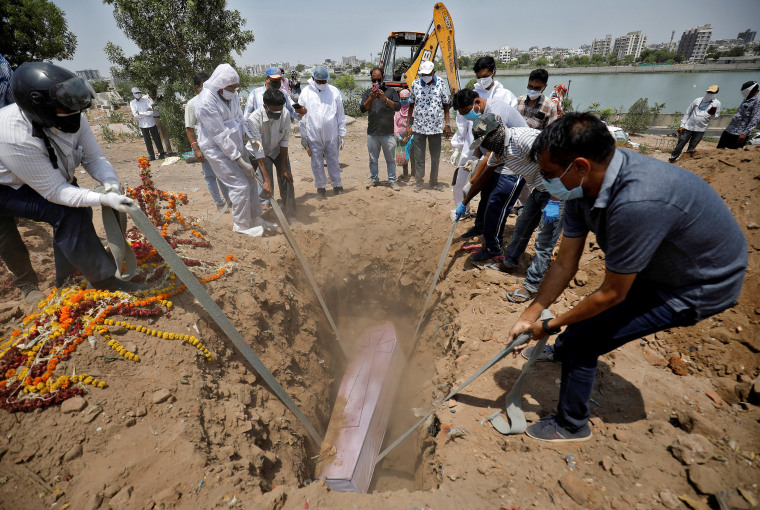 Image: People lower the body of 65-year-old Arnold Samuel Christian, who died from Covid-19, into a grave at a cemetery in Ahmedabad