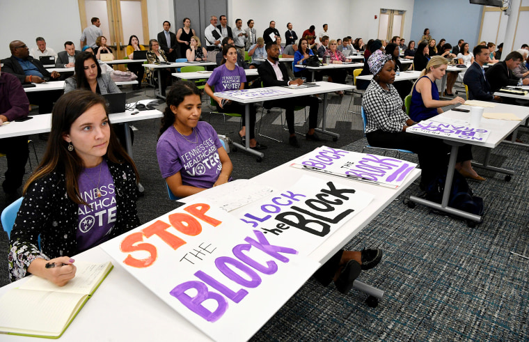 People from the Tennessee Justice Center hold signs at a public hearing on Oct. 1, 2019, in Nashville, Tenn., on Tennessee's request for block grant funding for Medicaid.