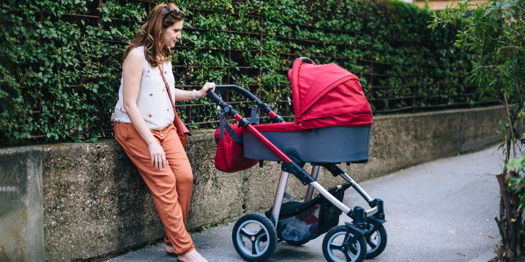 Image of a Mom pushing a baby in a red stroller, with a red diaper bag hanging on it