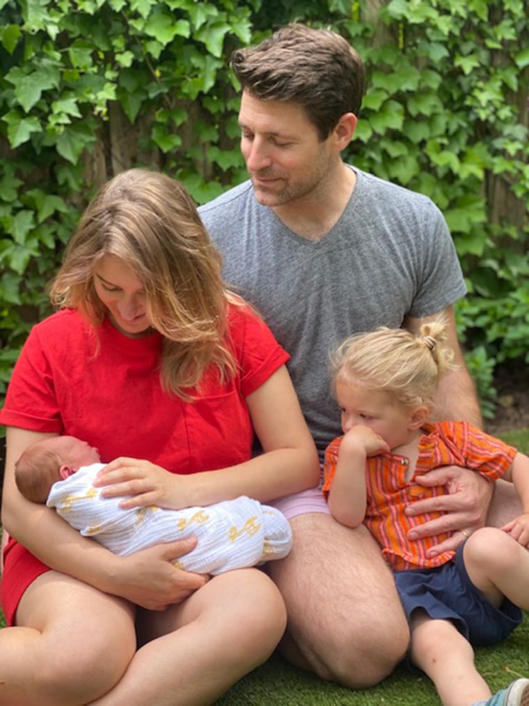 katy tur in a red dress holds her newborn baby sitting outside with her husband and son Teddy
