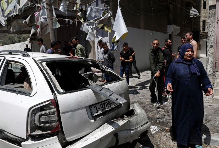 Image: Residents gather around a car that was hit in an Israeli airstrike that killed three people in the car, on the main road in Gaza City