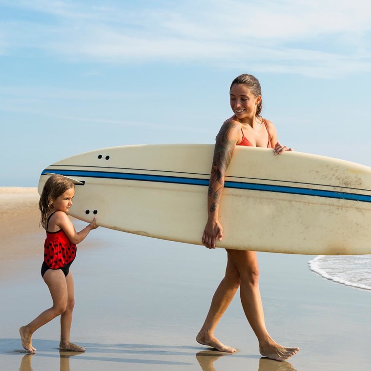 Mother and daughter walking on beach holding surfboard