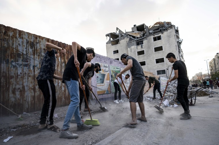 People clean the streets on Friday, beside a building that was damaged in an air-strike.