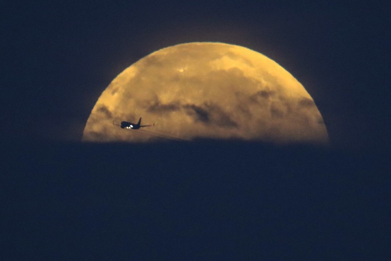 An airplane flies past as the Super Flower Blood Moon as it sets over Santa Monica, Calif., on May 26, 2021.