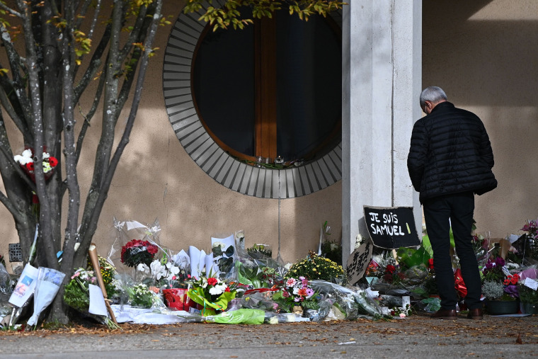 Image: A man looks at flowers laid outside the Bois d'Aulne secondary school outside of Paris in homage to slain history teacher Samuel Paty, who was beheaded by an attacker for showing pupils cartoons of the Prophet Mohammed in his civics class.