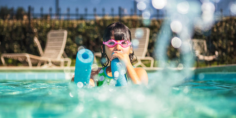 Little girl wearing goggles squirting water with a pool noodle