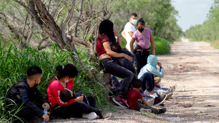 Families and small children from Central America and Mexico sit in a field near the Rio Grande river after being apprehended by U.S. Border Patrol agents on on May 25, 2021.