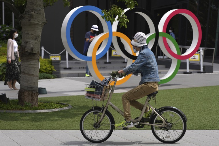 Image: A woman rides a bicycle near the Olympic Rings Wednesday, June 2, 2021, in Tokyo.
