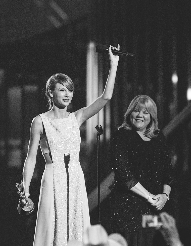 Taylor Swift in a formal gown waves to the crowd as her mother looks on
