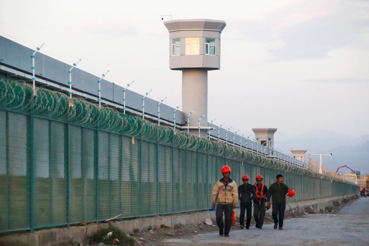 Image: Workers walk by the perimeter fence of what is officially known as a vocational skills education centre in Dabancheng in Xinjiang Uighur Autonomous Region, China.