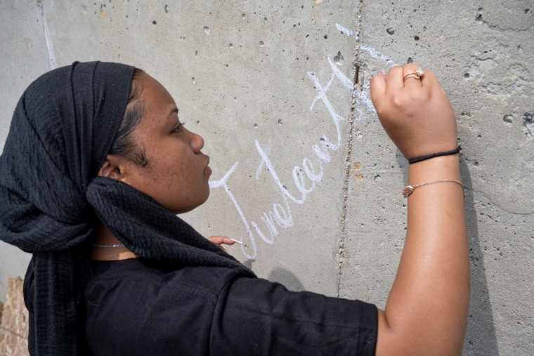 A young person writes Juneteenth on a wall in chalk in Louisville, Kentucky.