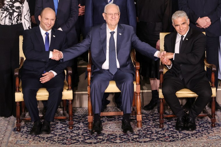 Image: Israel's President Reuven Rivlin between Prime Minister Naftali Bennett and Foreign Minister Yair Lapid as they pose for a group photo with ministers of the new Israeli government, in Jerusalem