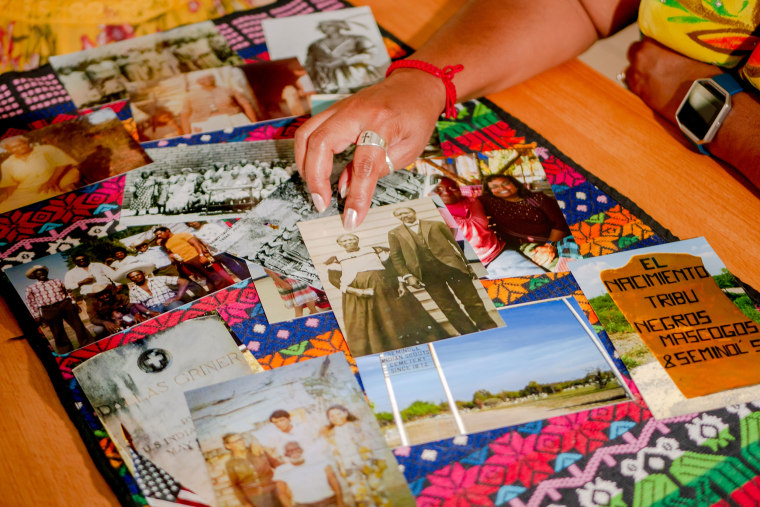 Historical photos displayed on a table including in the center a black and white photo of Corina Torralba Harrington's great grandmother, Effie Payne, whose Mexican name was Felipa Valdes, with her son, Ned Griner, whose Mexican name was Manuel Torralba, in Brackettville, Texas. Bottom right, is a photo of painted rock that marks the direction to Nacimiento de los Negros, Mexico where Juneteenth brings together descendants of Black Seminoles.