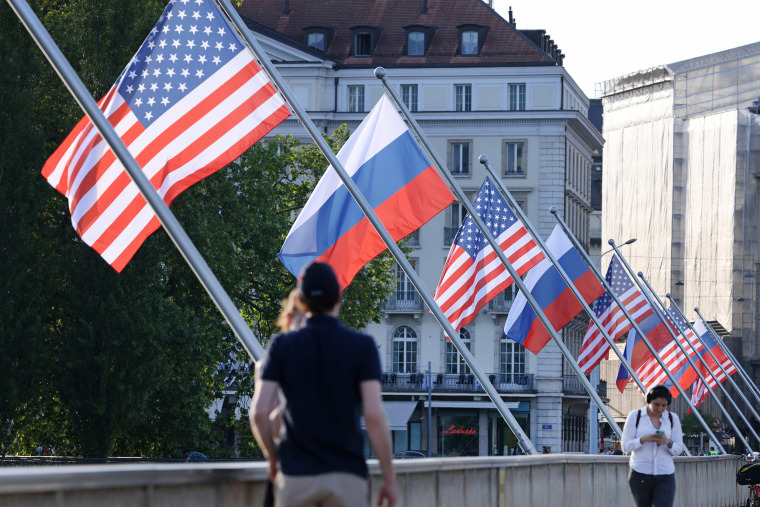 Image: People walk under Russian and American flags on a bridge in the city center prior to a meeting between U.S. President Joe Biden and Russian President Vladimir Putin