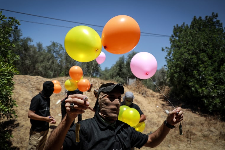 Image: Masked Palestinian supporters of the Al-Nasir Salah Al-Din Brigades prepare incendiary balloon