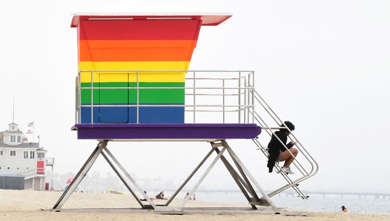 A woman sits on the steps to the new rainbow-colored Pride lifeguard tower on June 16, 2021, in Long Beach, Calif.