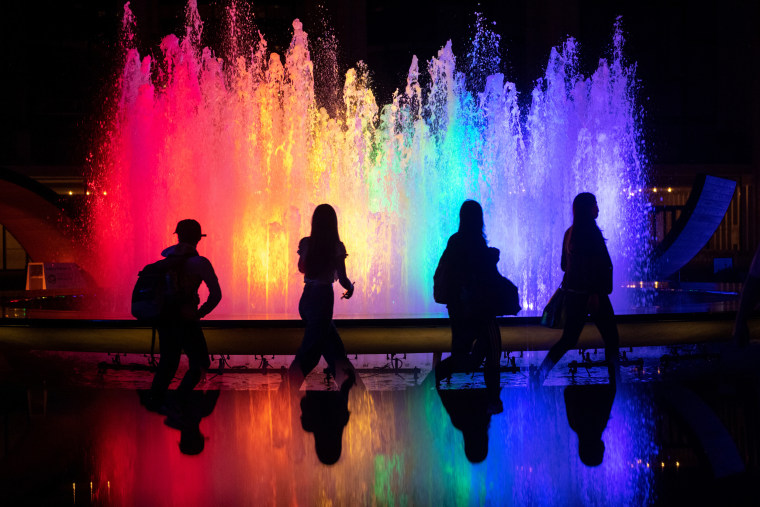 People walk past the fountain at Lincoln Center for the Performing Arts lit up in Pride colors on June 2, 2021, in New York.