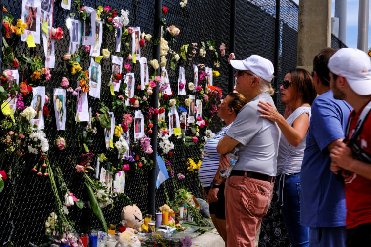 People mourn at the memorial site created by neighbors in front of the partially collapsed building where the rescue personnel continue their search for victims in Surfside, Fla., on June 26, 2021.