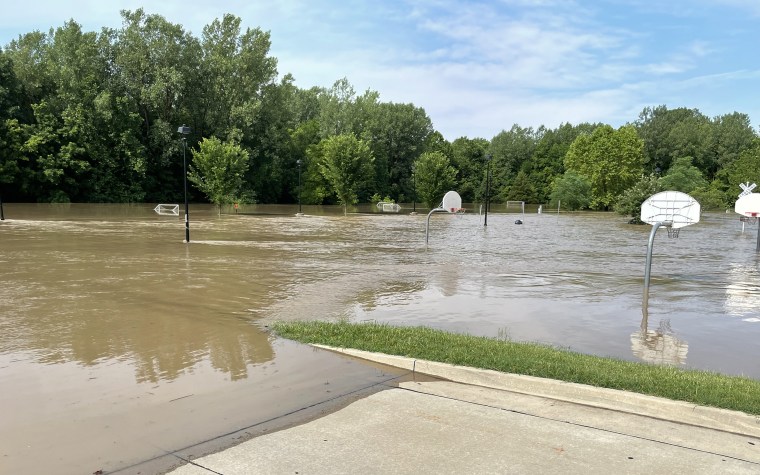 A park underneath brown floodwater under a blue sky