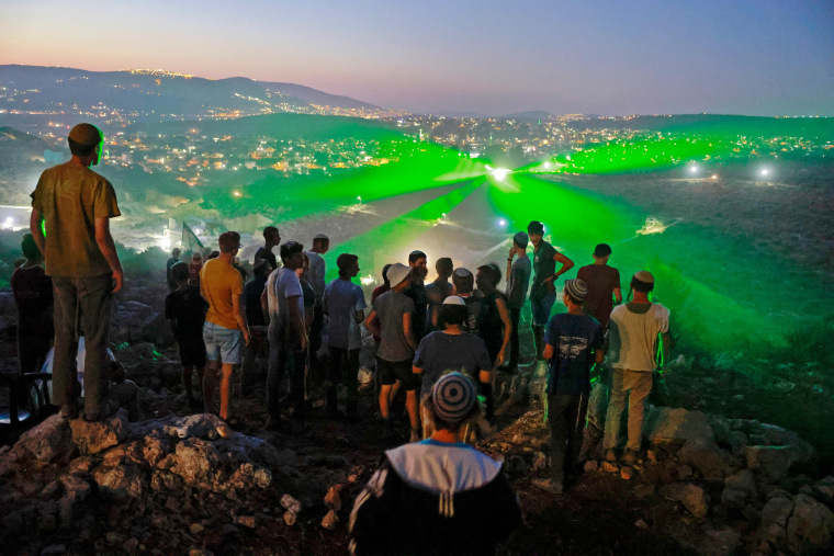 Israeli settlers in the outpost of Eviatar look on as Palestinian protestors flash laser beams towards them earlier this week. 