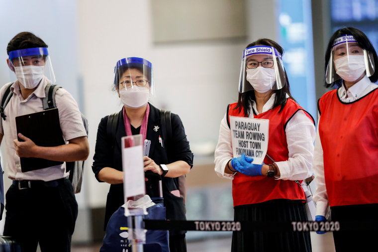Image: Staff wearing face masks and shields wait for the arrival of foreign athletes at Haneda Airport ahead of Tokyo 2020 Olympic Games, in Tokyo