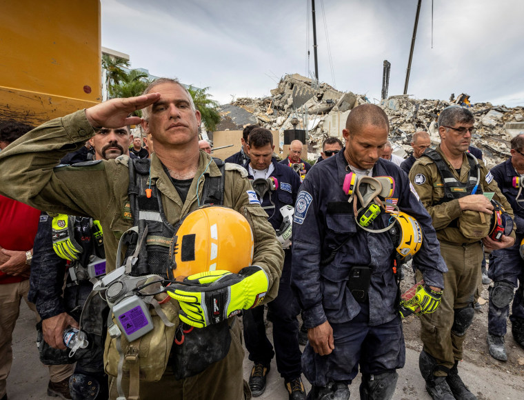 Image: Search and rescue team stands in front of rubble that once was Champlain Towers South during prayer ceremony and a moment of silence in Surfside