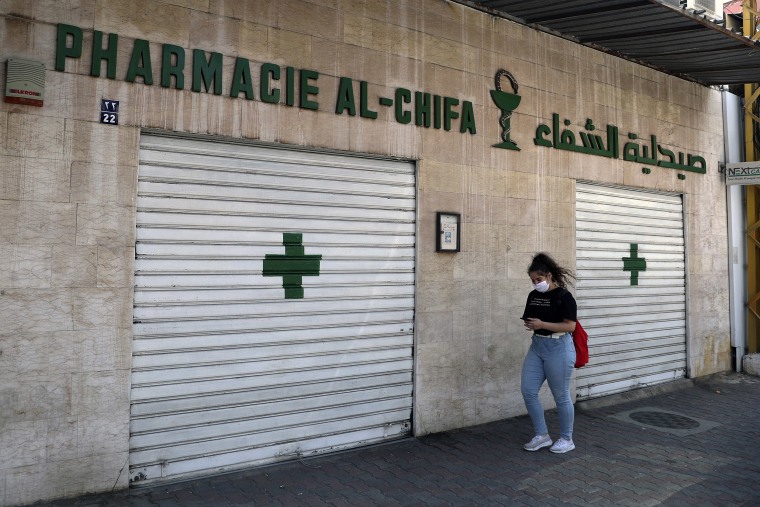 Image: A woman passes by a closed pharmacy in Beirut.