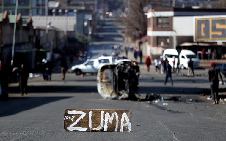 Image: The remains of a burnt car and a sign block the road after stick-wielding protesters marched through the streets in Johannesburg.