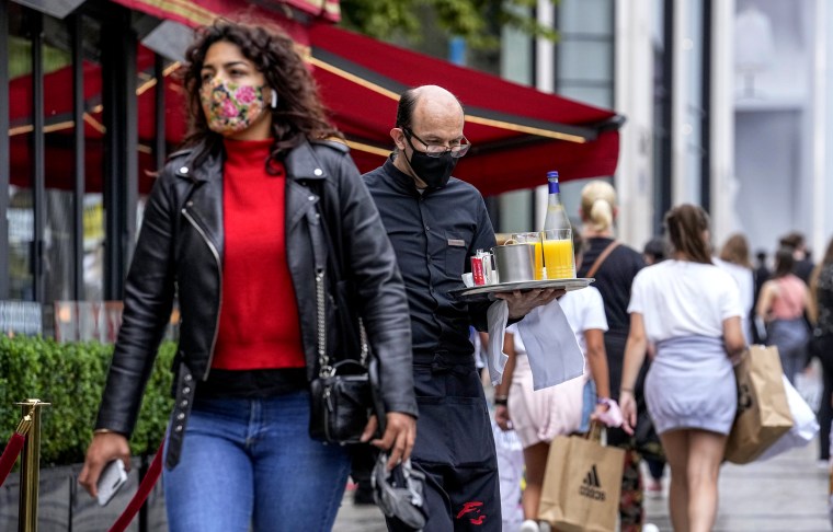 Image: A waiter wearing a face mask to protect against coronavirus serves customers at the Champs Elysees avenue in Paris on July 12, 2021.