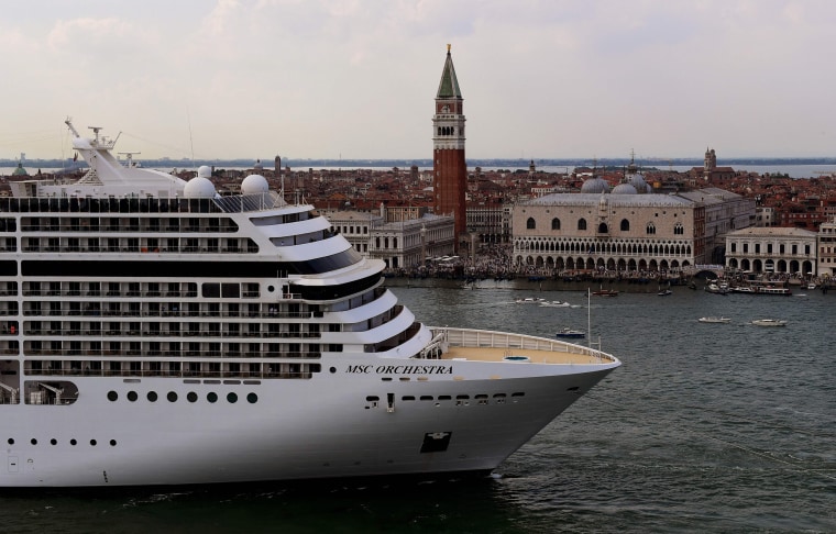 Image: Tugboats escort the MSC Orchestra cruise ship across the basin past the Bell Tower and the Doge's palace as it leaves Venice