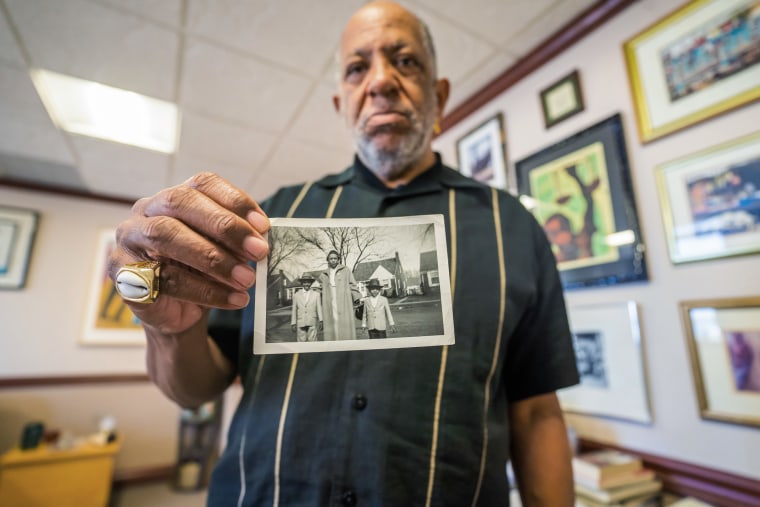 Jeffrey Edison holds a photo of himself with his mother and brother in the front yard of his childhood home.